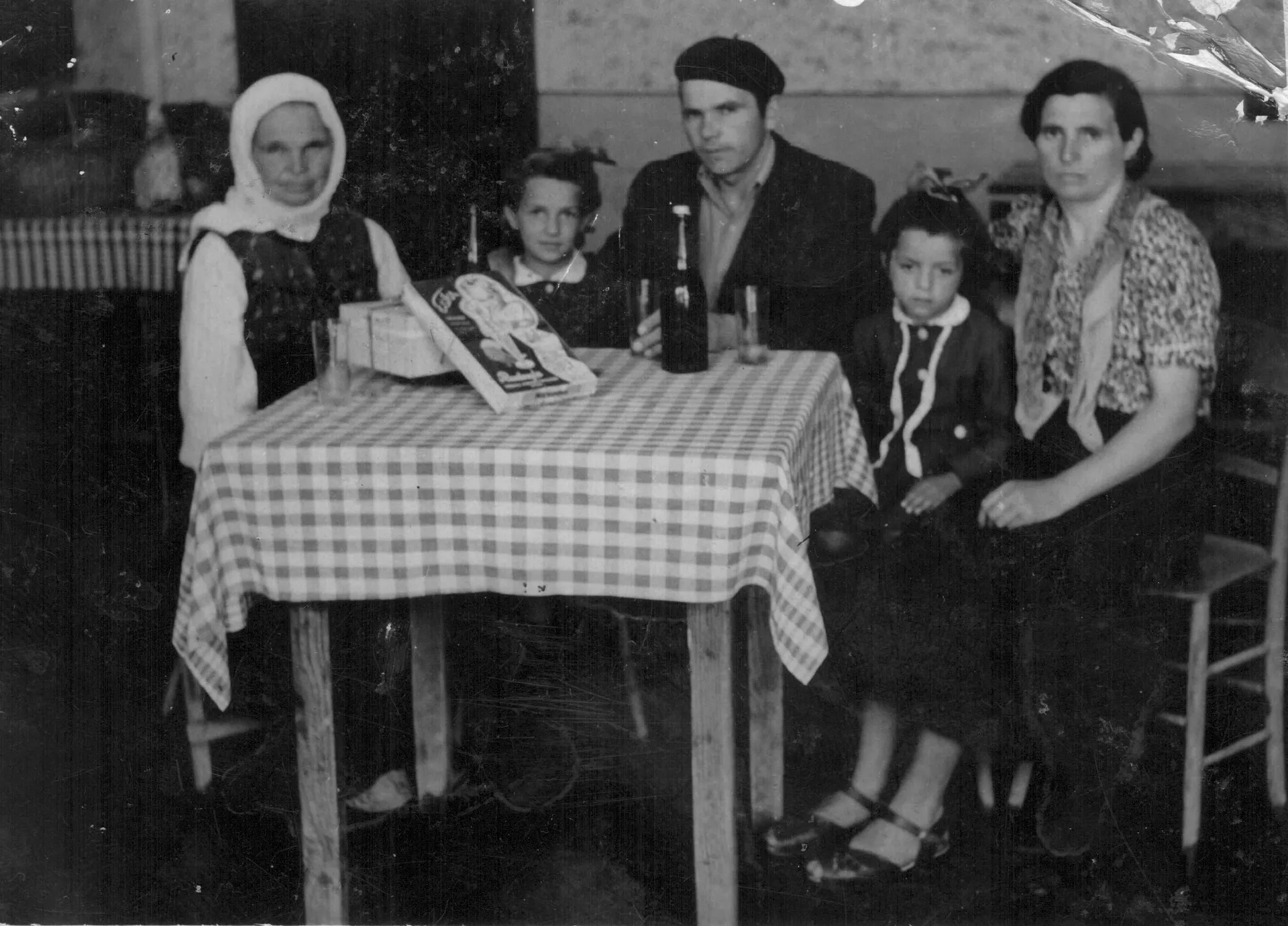 Crno-bela porodična fotografija iz 1955: porodica za stolom sa kariranim stolnjakom
