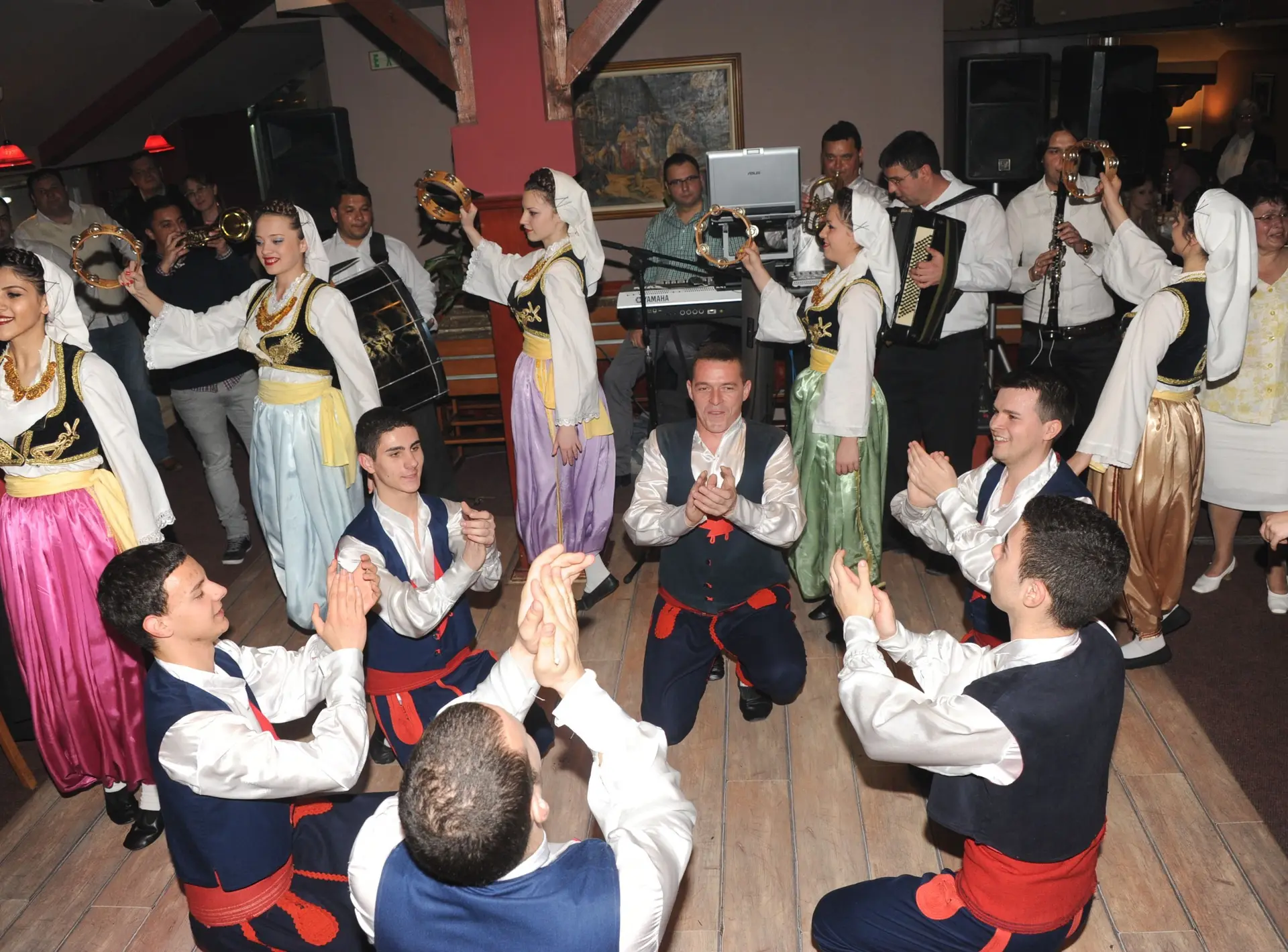 Igrači u nošnjama kleče u krugu i tapšu, igračice podižu defove
